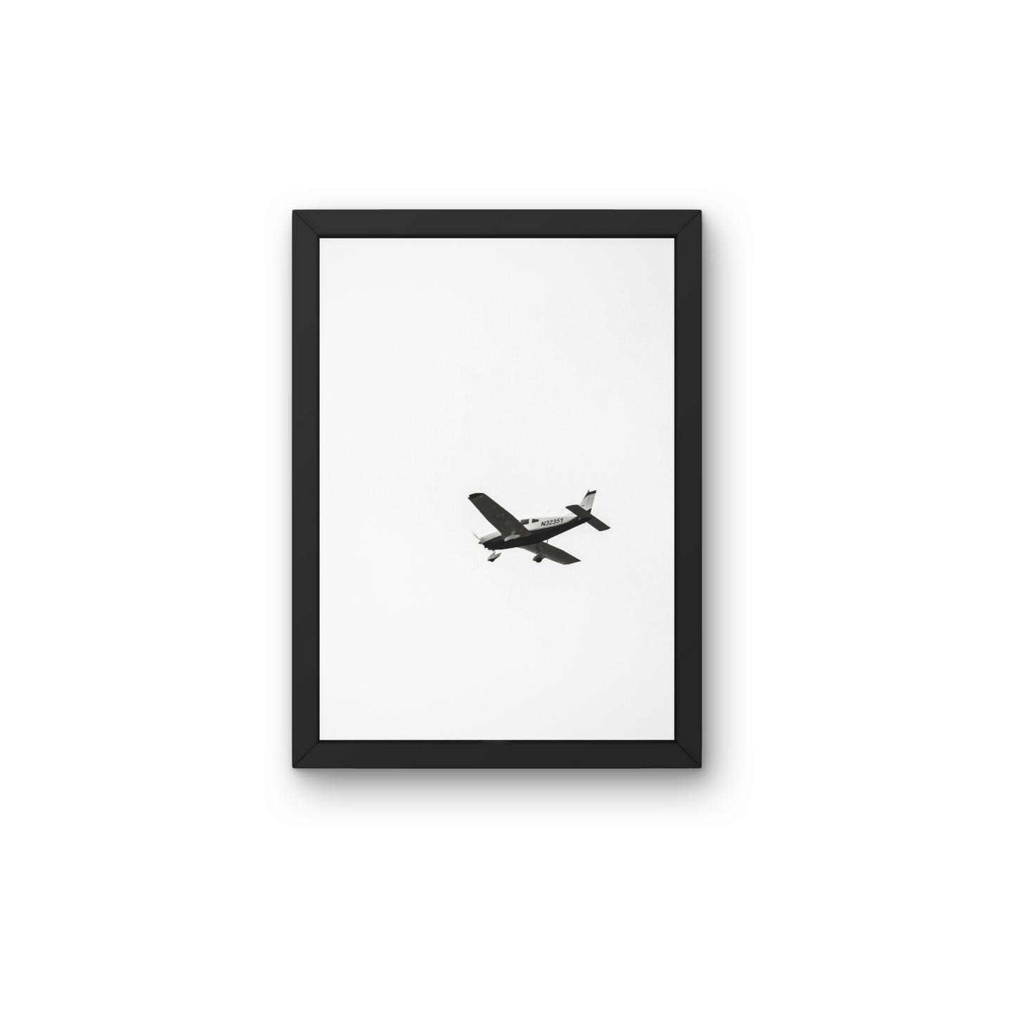 Minimalist wall art featuring an airplane in mid-air against a white background."




